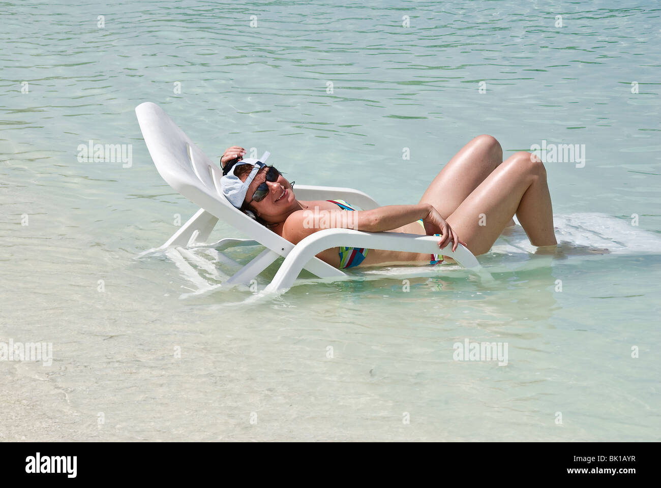 Young adult female lying on a recliner that is in the sea relaxing sunbathing in the sun Stock Photo