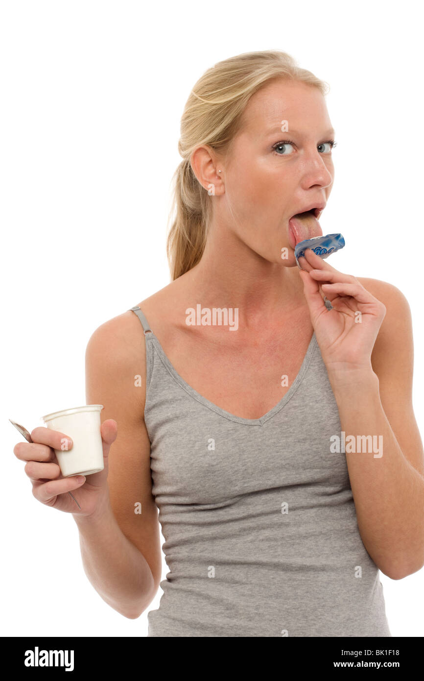 portrait of a young caucasian woman who licks the lid of a pot of yogurt and looking at camera Stock Photo