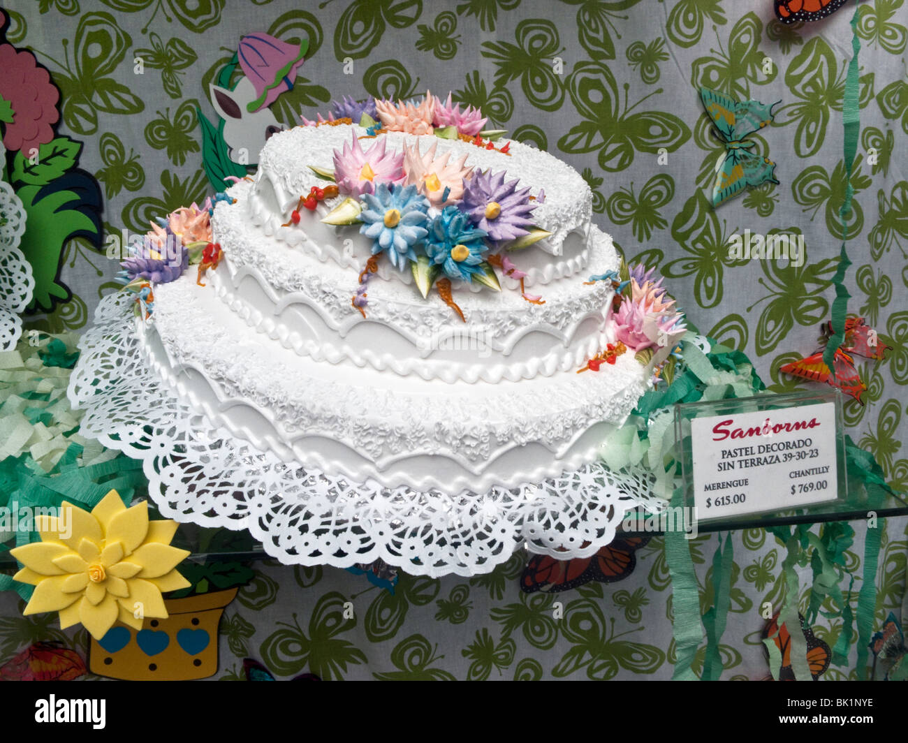 elaborate tiered cake with white icing decorated with large realistic colored sugar flowers in Sanborn's window Mexico City Stock Photo