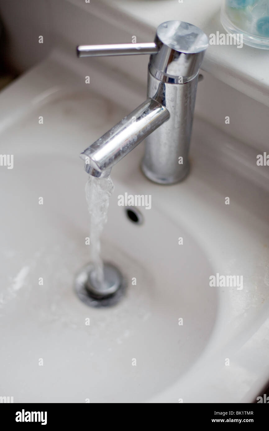 Water Running From A Tap Into A White Bathroom Sink Stock Photo