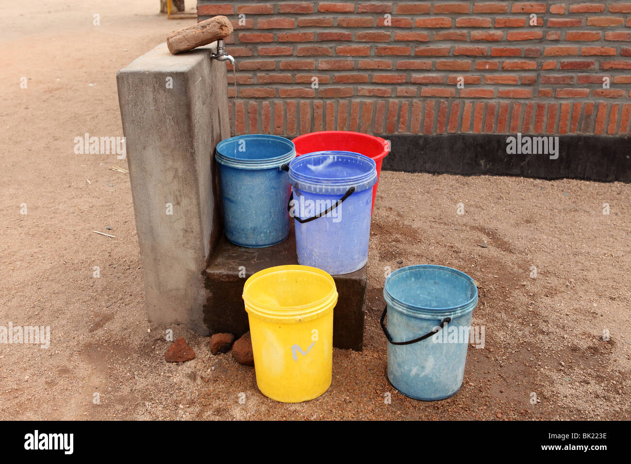 Colorful buckets sit next to a tap where people fill their buckets for daily water use in a communal water station in Malawi Stock Photo