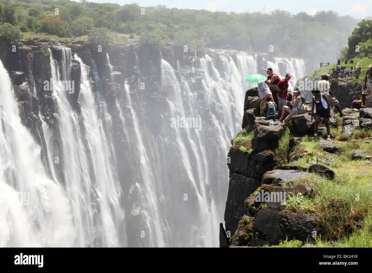 Tourists stand on a cliff and look at the Victoria Falls on the Zimbabwe side Stock Photo