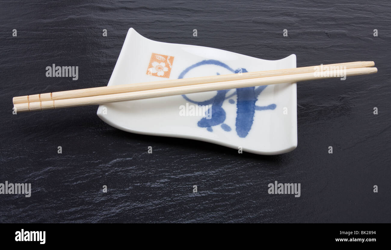 Pair of wood or bamboo Chopsticks arranged on rest against dark slate background. Stock Photo