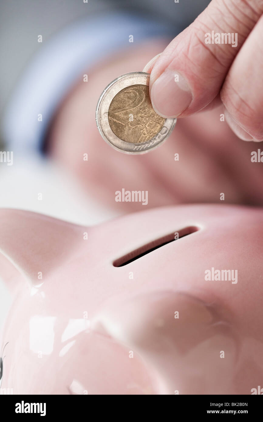 Hand putting coin into piggy bank Stock Photo - Alamy
