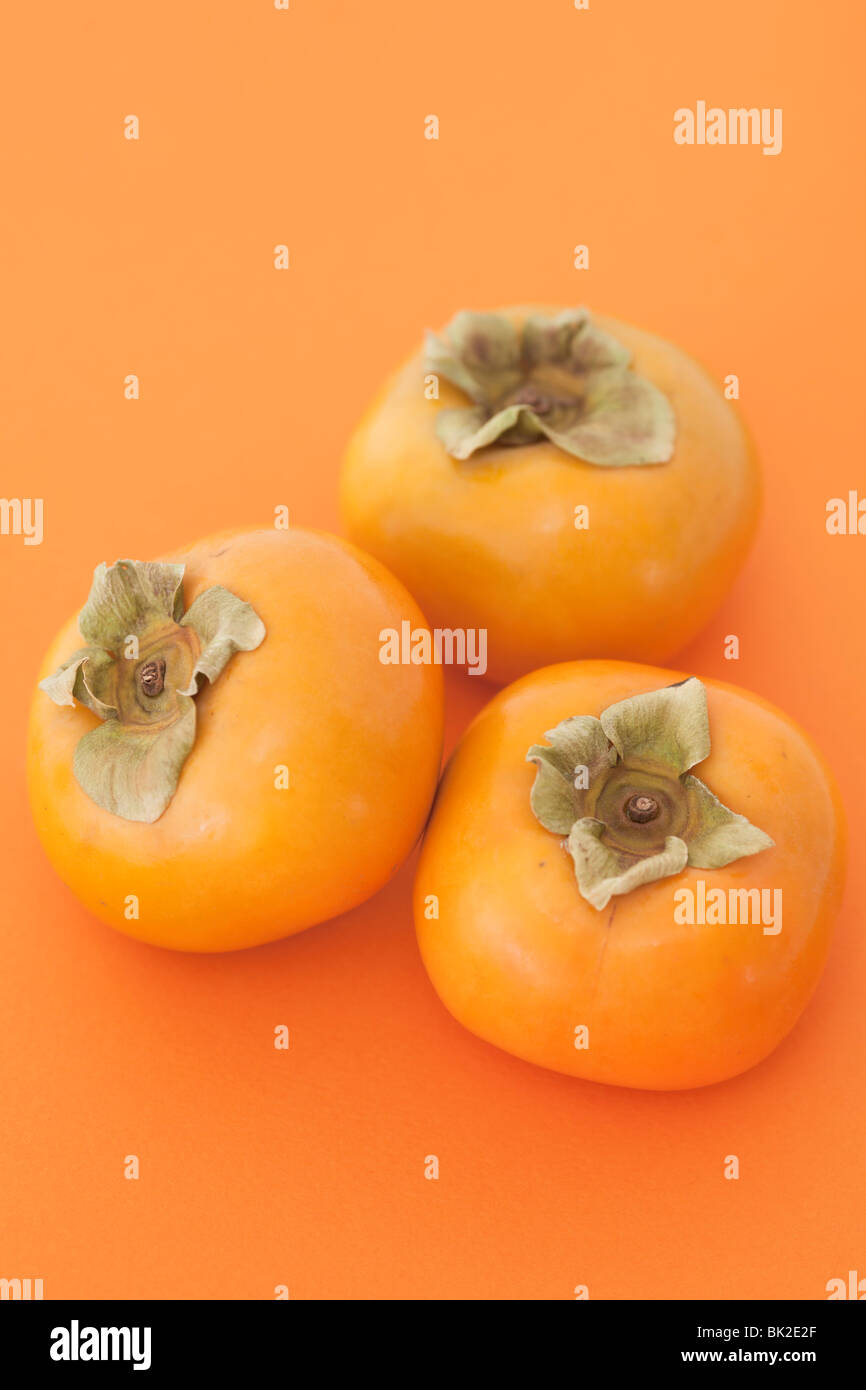Three persimmon fruits on a coloured background. Stock Photo