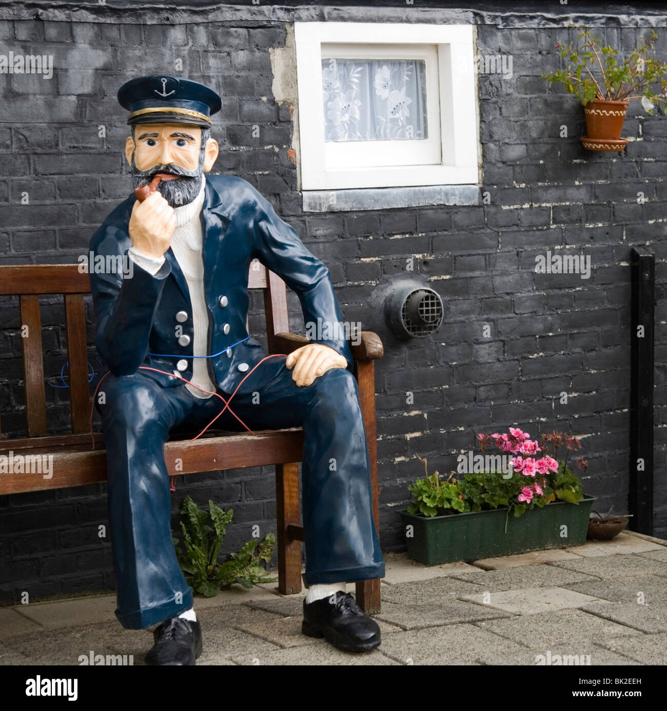 Navy blue statue of sailor sitting on a garden bench smoking a pipe