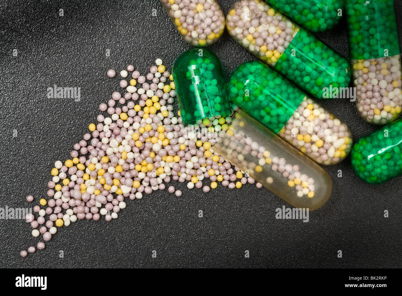 Hard-shelled medicinal capsules with the tiny medicine pellets spilled out showing the size Stock Photo