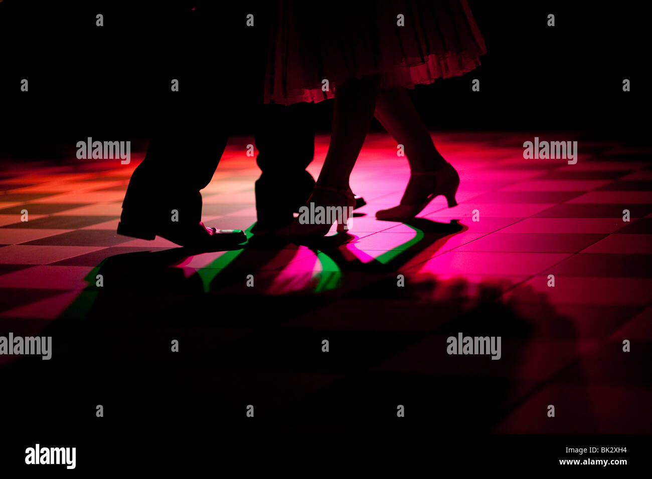 2 pair of feet dancing shown in the colored light on a dancefloor Stock Photo