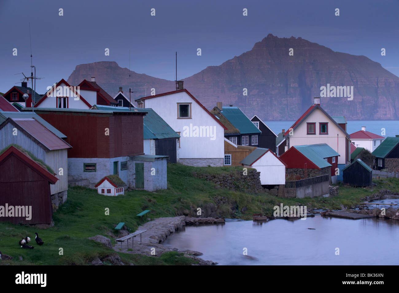 Houses at Gjogv at twilight, with view of Kalsoy cliffs of Nestindar, 788m, and Borgarin, 537m, Eysturoy, Faroe Islands Stock Photo