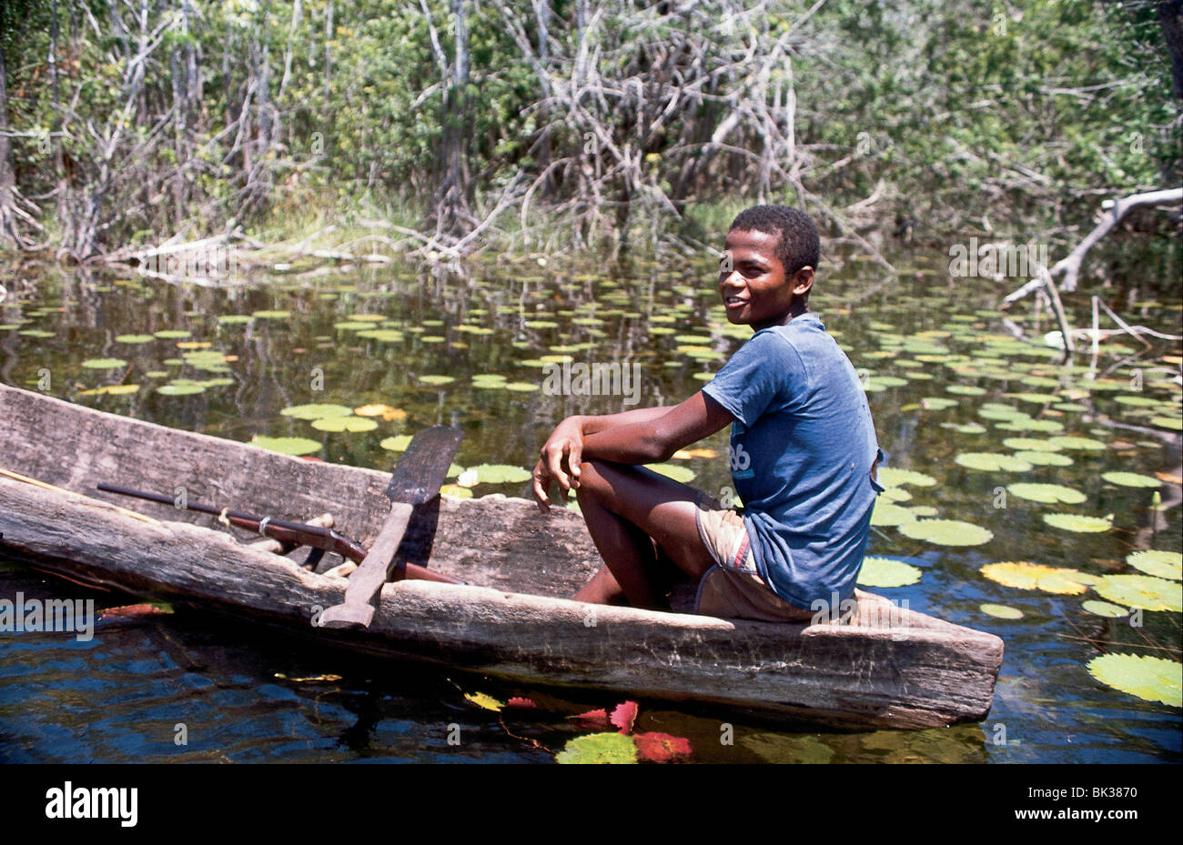 A boy sitting in a dug out canoe with a rifle and homemade paddle, Belize Stock Photo