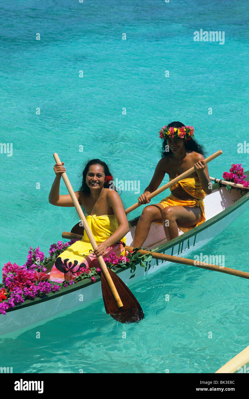 Two young women paddle an outrigger canoe across a lagoon on the island