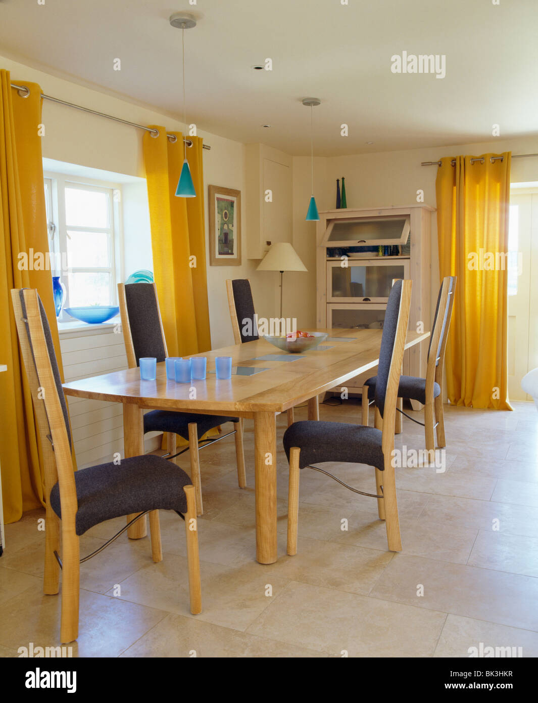 Yellow curtains and limestone flooring in modern dining room with tall