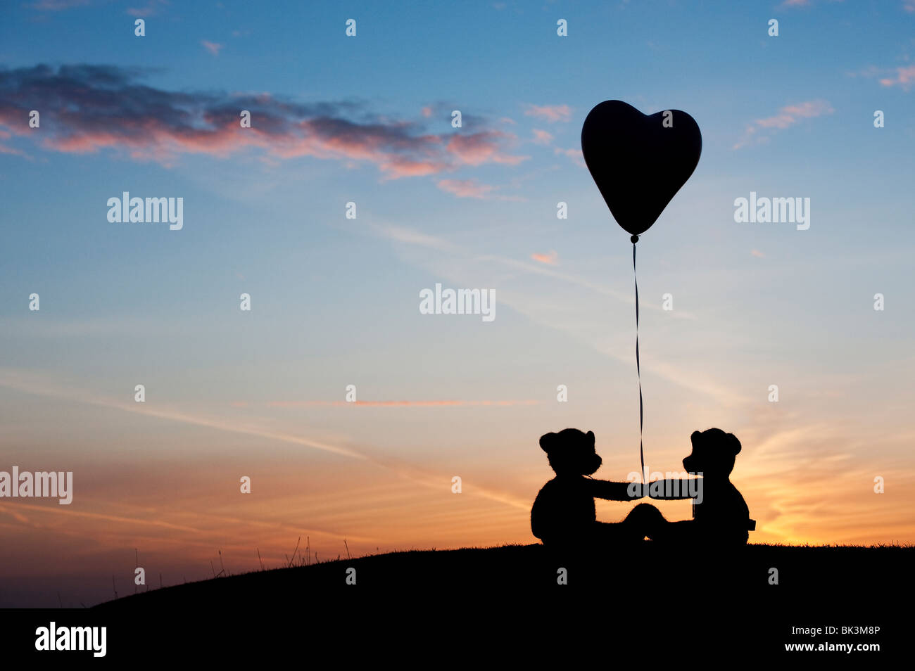 Two teddy bears holding a heart shape helium balloon at sunrise. Still ...