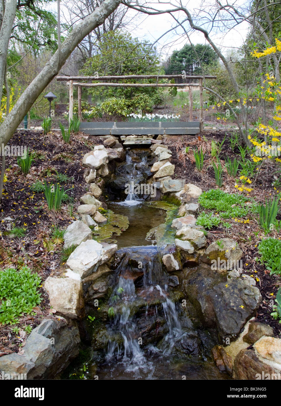 A garden bridge over a flowing stream with small waterfalls. Stock Photo