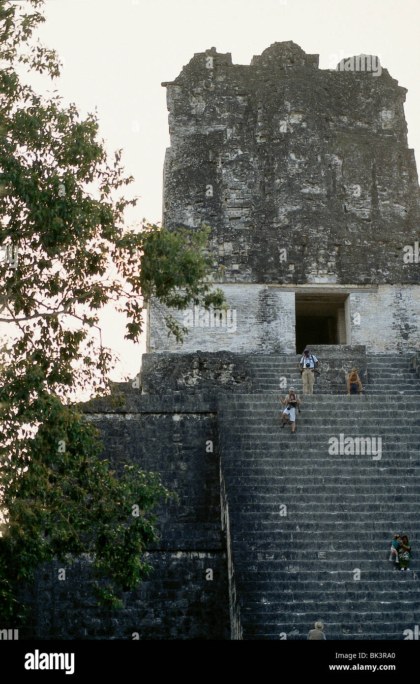 Tourists climbing the steep steps of an ancient Mayan temple pyramid at