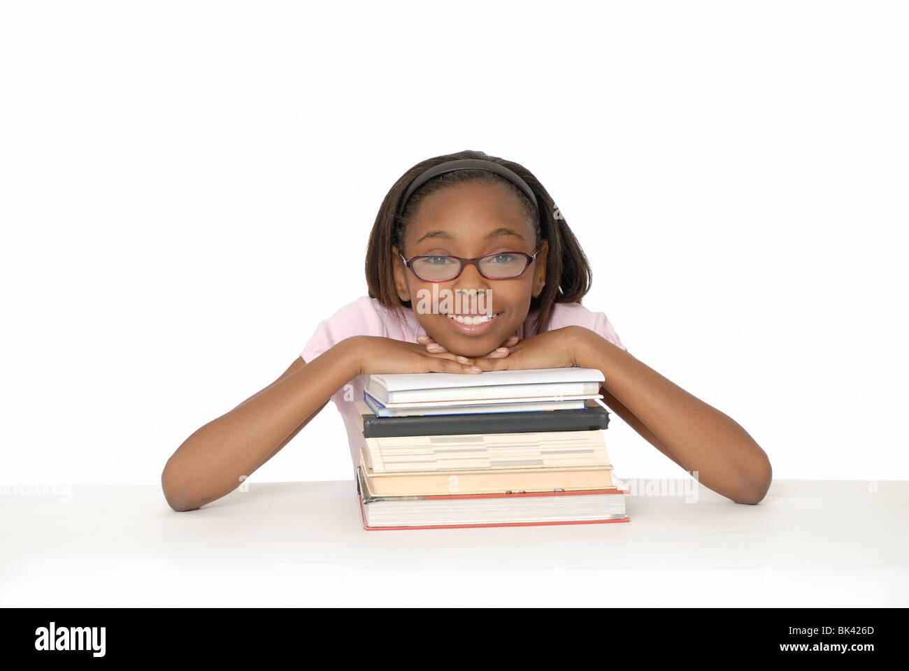 Ten year old girl smiling and leaning on a stack of books. Stock Photo