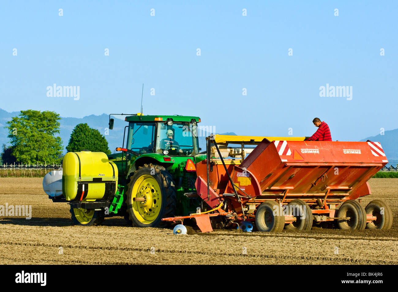 Planting potatoes with a 4 row planter being pulled by a John Deere tractor in the spring in Skagit County, Washington Stock Photo