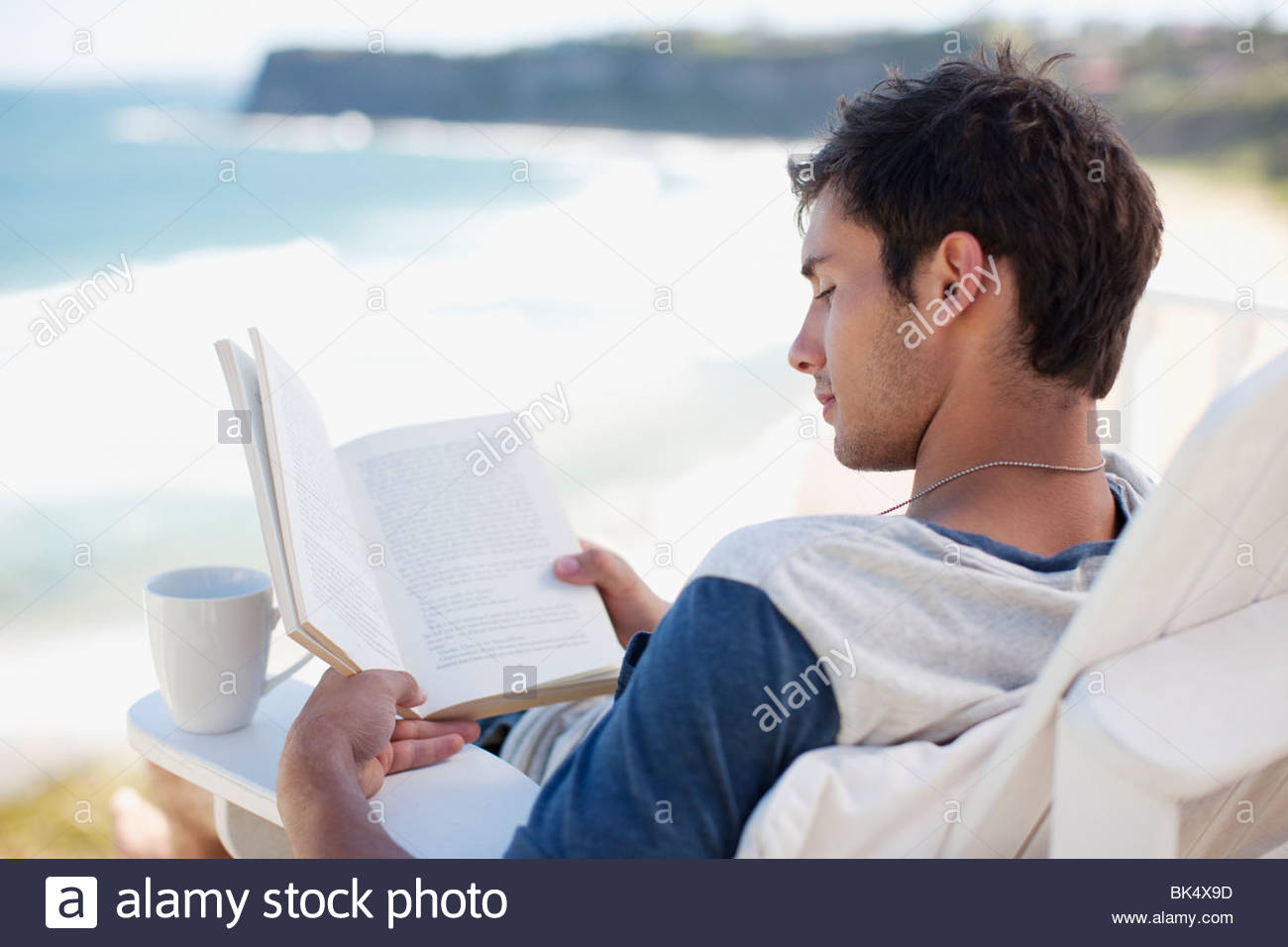 Man With Coffee Cup Reading Book In Deck Chair Overlooking