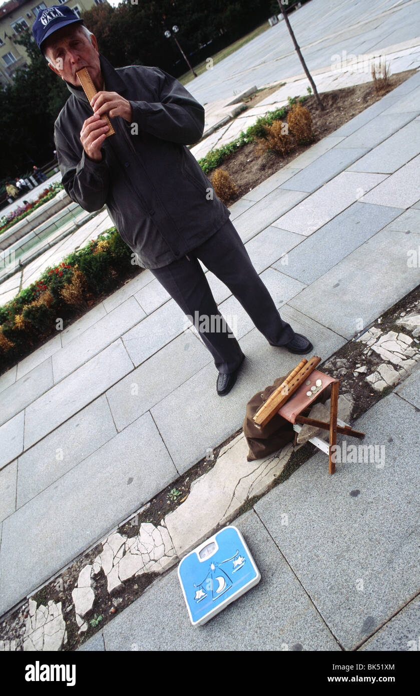 Street musician plays the flute in a park in front of the National Palace of Culture in Sofia, Bulgaria. Passersby can also weig Stock Photo