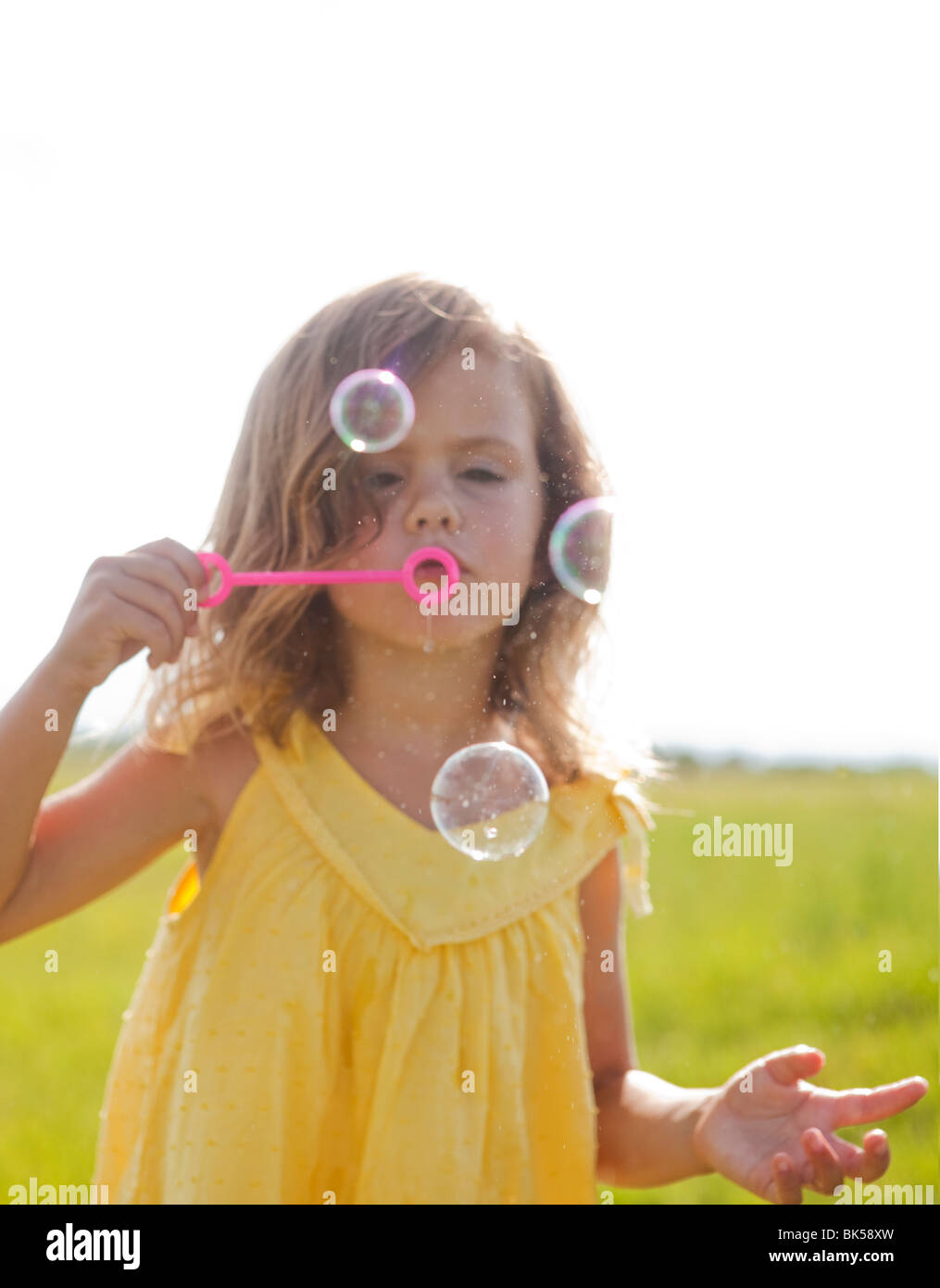Young girl in yellow sundress blowing bubbles Stock Photo