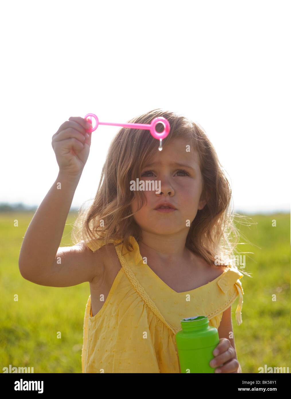Young girl in yellow sundress blowing bubbles Stock Photo