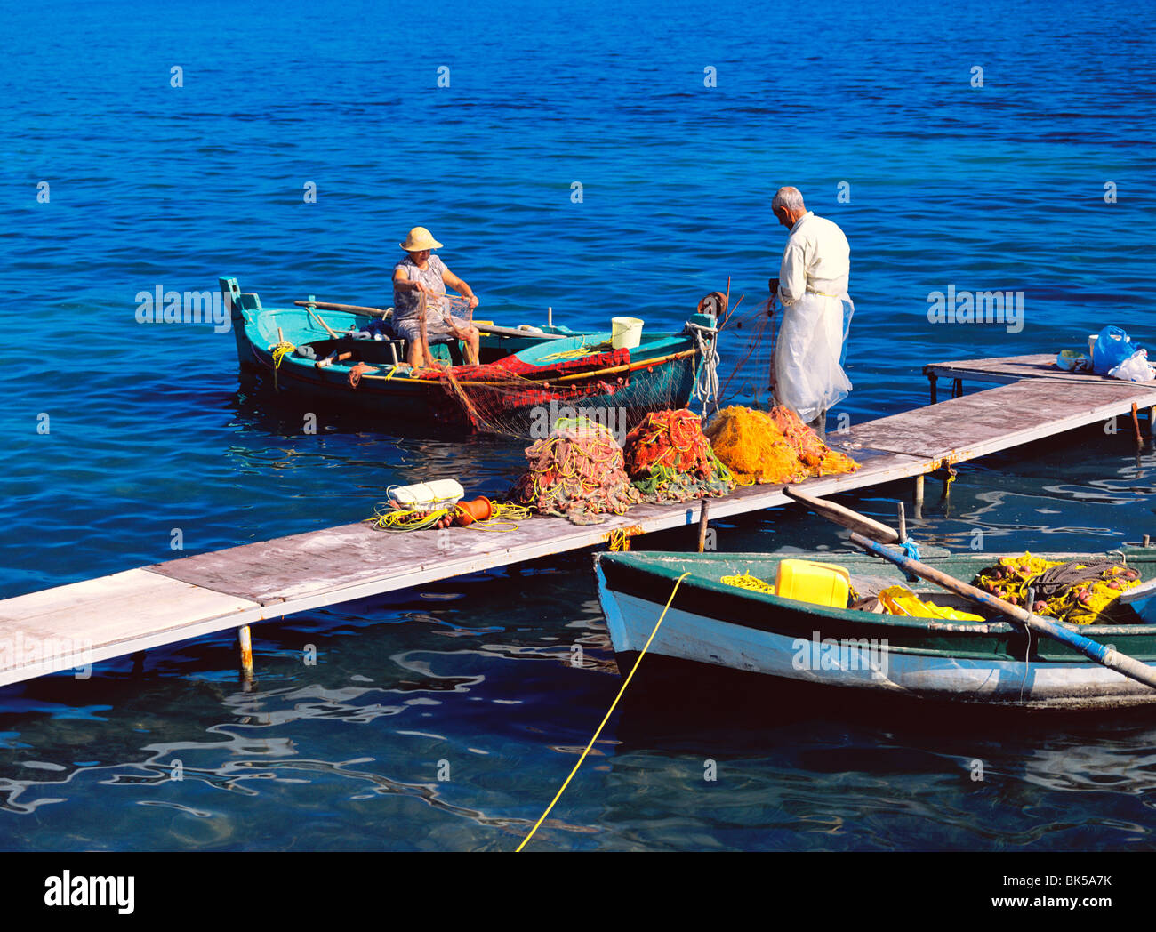 Fisherman and his wife cleaning the fishing nets in boat and jetty, Corfu, Greek Islands, Greece, Europe Stock Photo