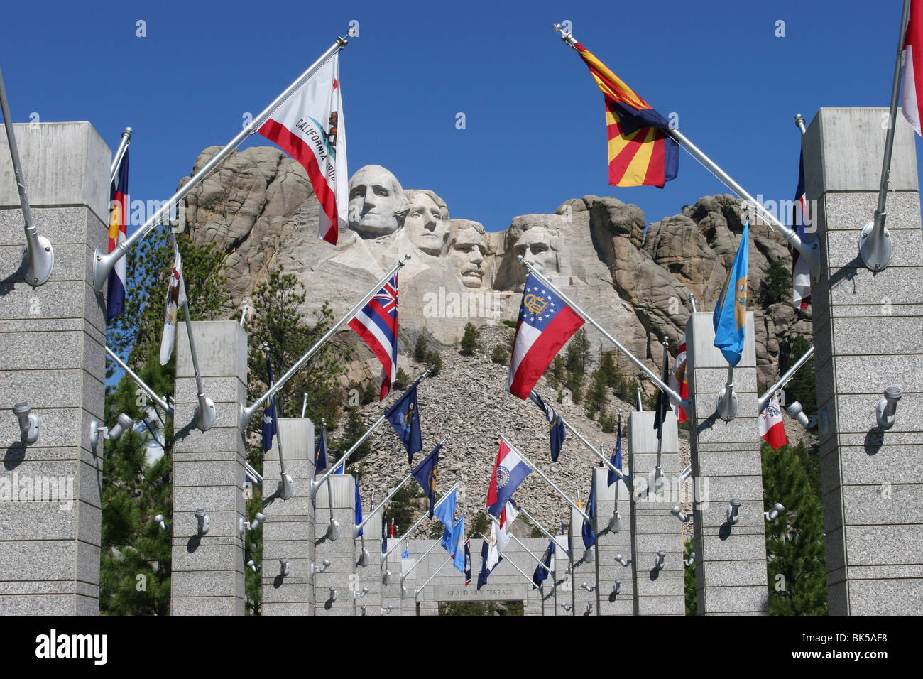 Flags on columns with sculptures former US presidents in background Mt Rushmore National Monument Black Hills South Dakota USA Stock Photo