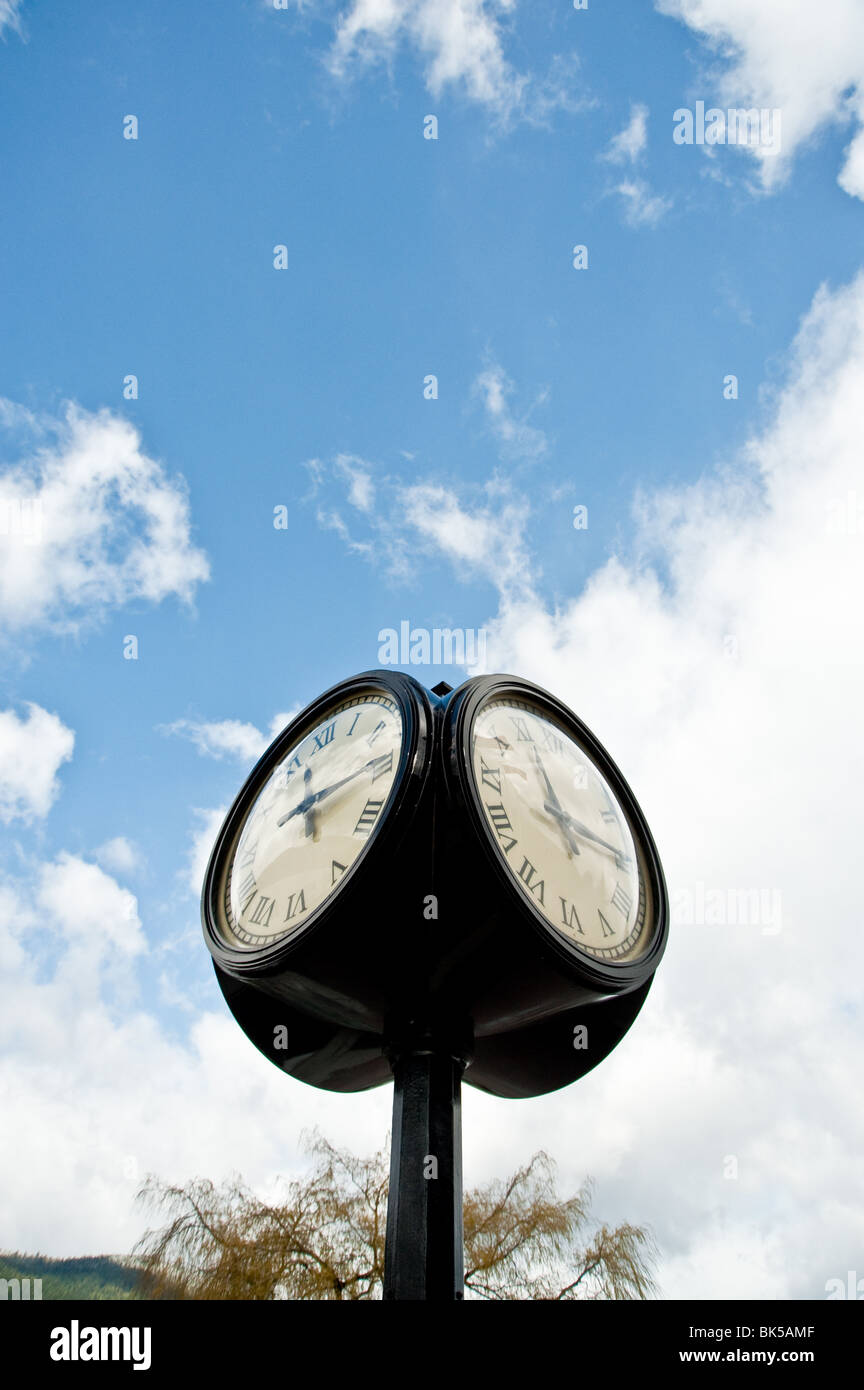 A big  four sided street clock on a street corner with blue sky in the background Stock Photo