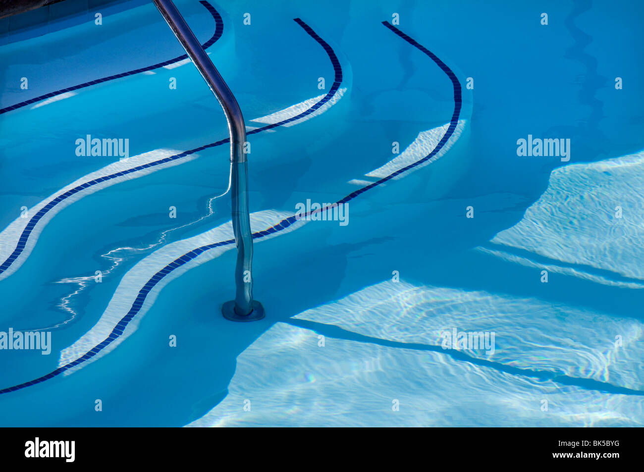 Curved stair steps and safety rail in blue water of swimming pool Stock Photo