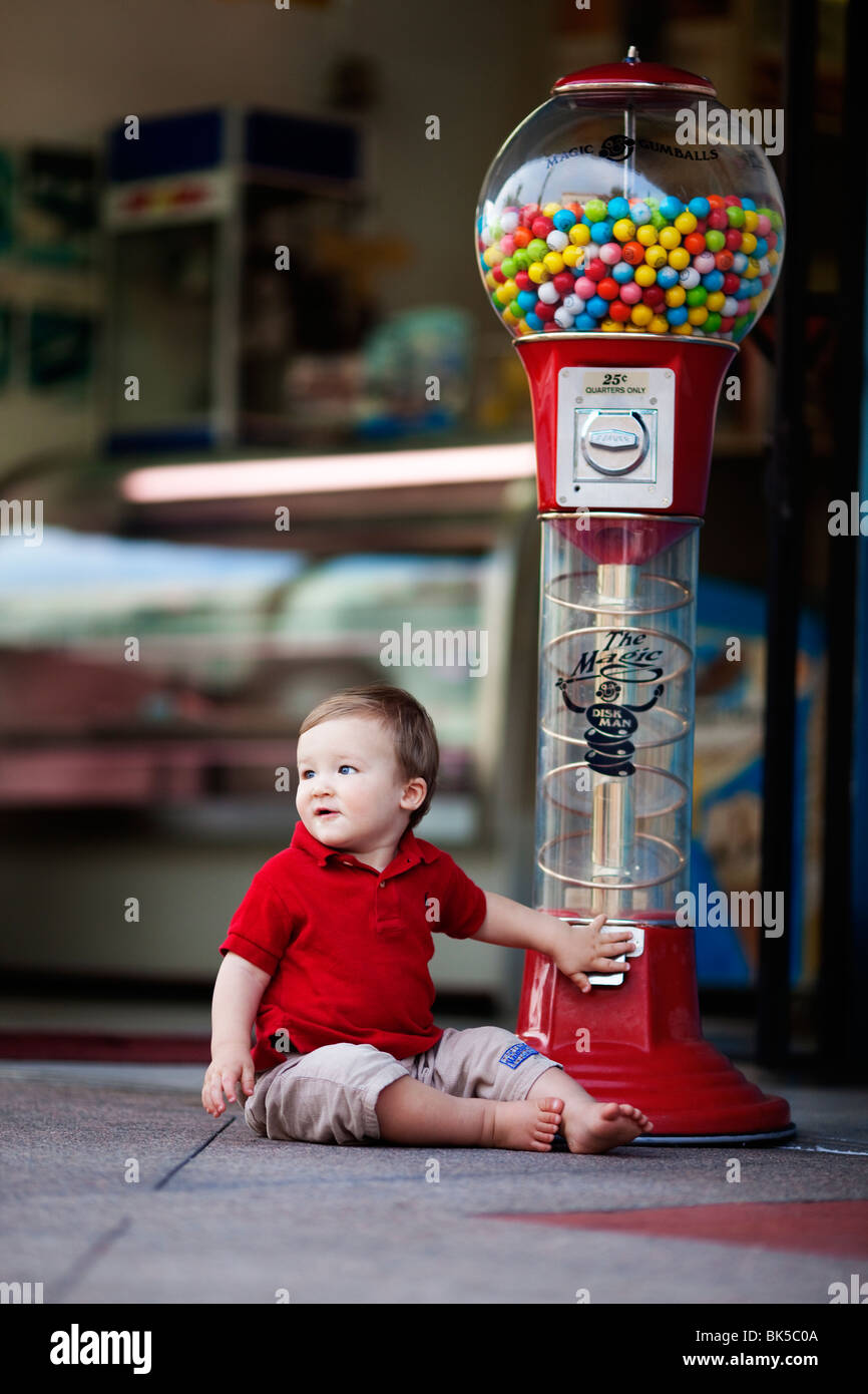 Young boy sitting by large gumball machine Stock Photo