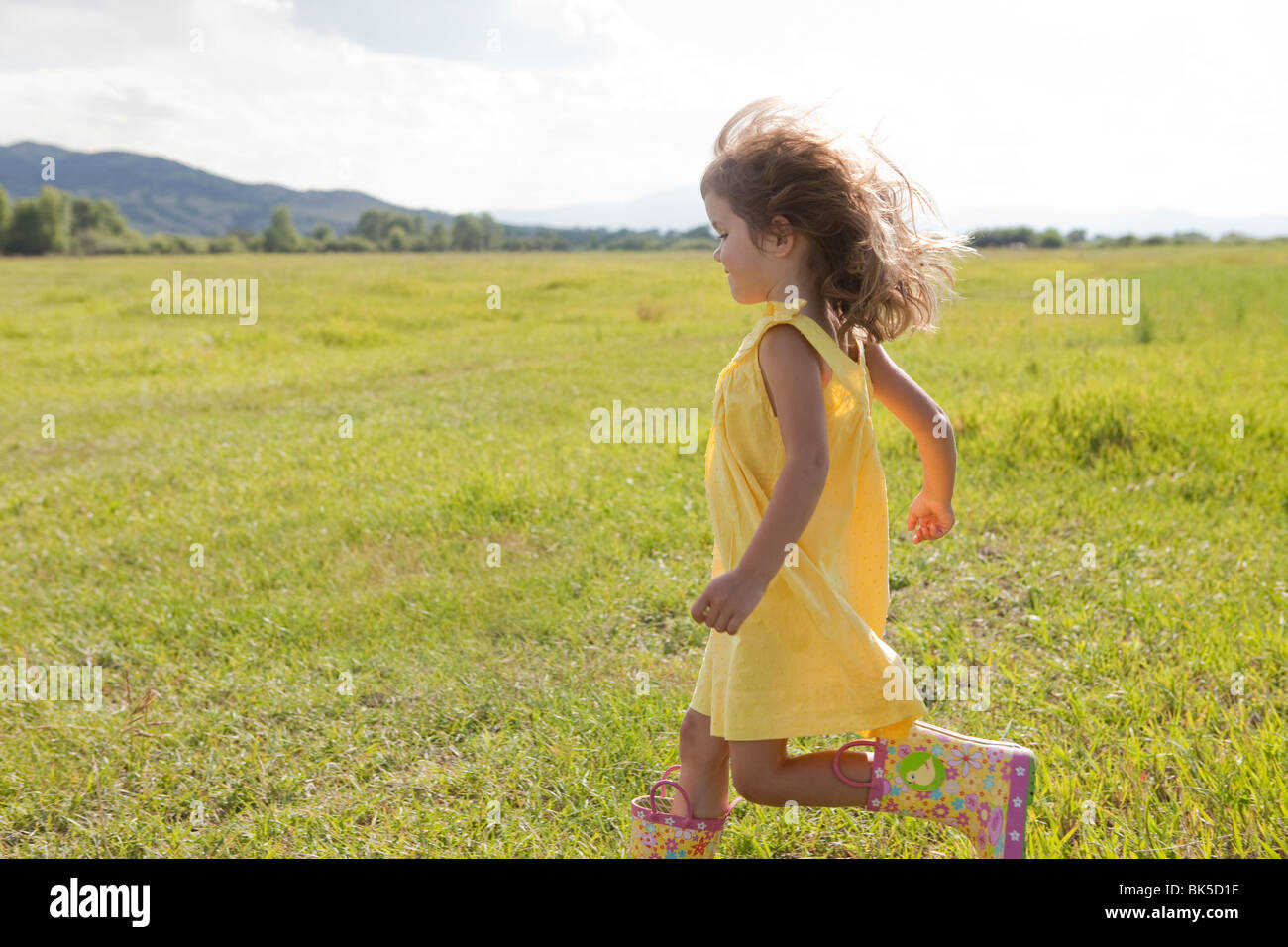 Young girl in yellow sundress running in field Stock Photo