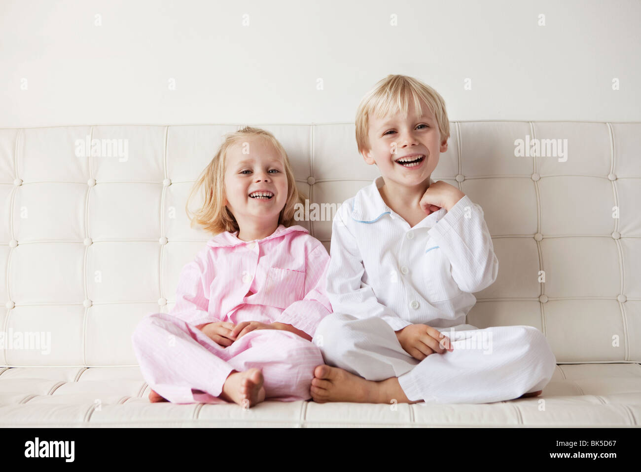 Young children in their pajamas sitting on the sofa Stock Photo