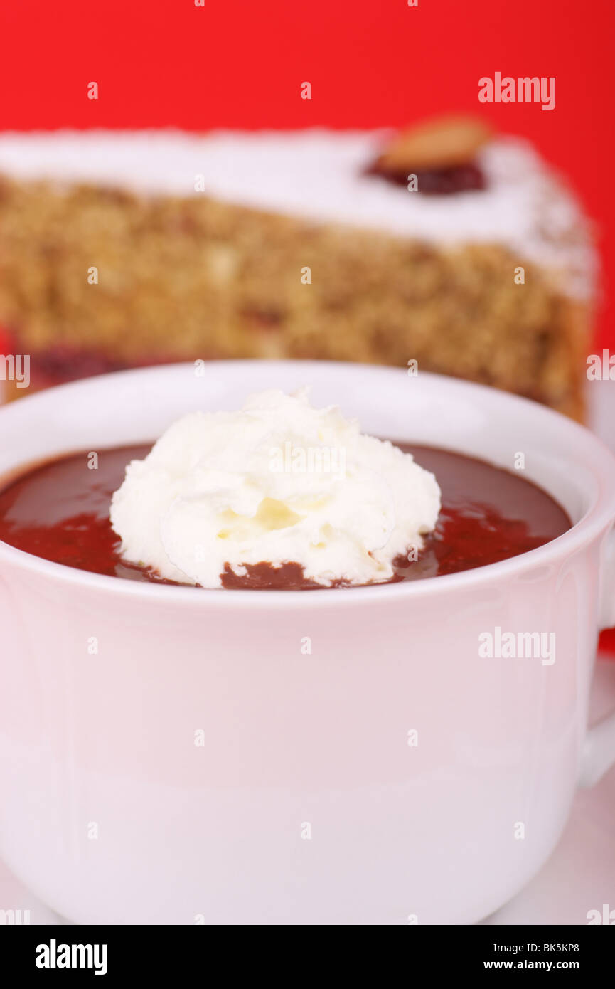A cup of hot chocolate with whipped cream and a piece of buckwheat cake in the background. Stock Photo