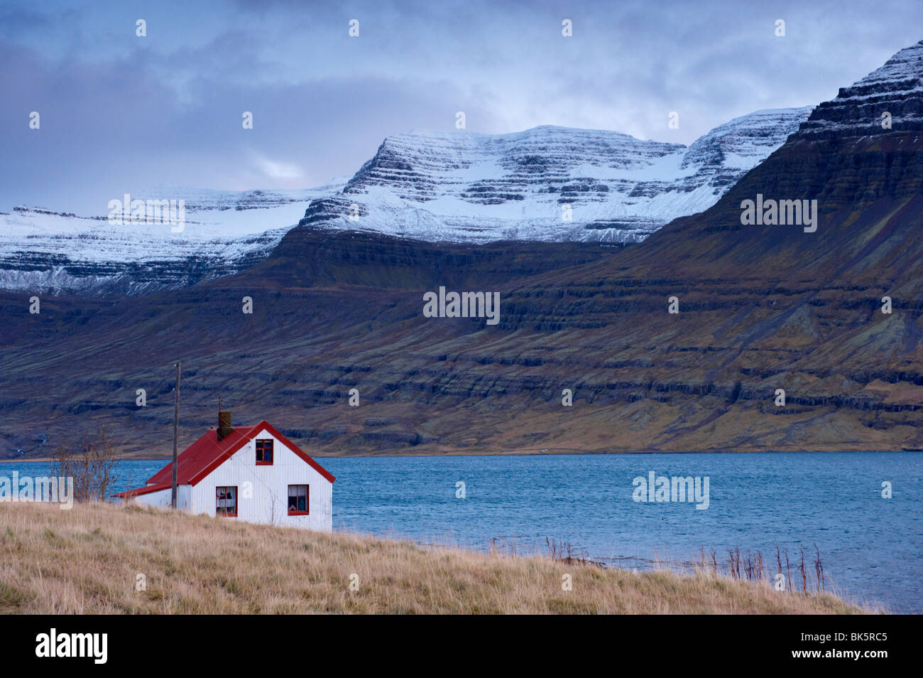 Red-roofed house and snow-capped mountains in Reydarfjordur fjord, East Fjords, Iceland, Polar Regions Stock Photo