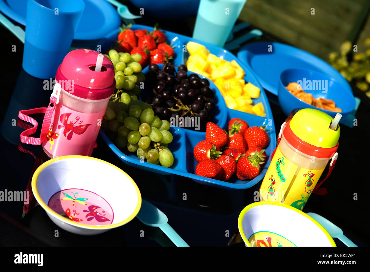 Outdoor meal or picnic on a black table with blue plastic bowls, cups, and jugs with fruit and salad Stock Photo