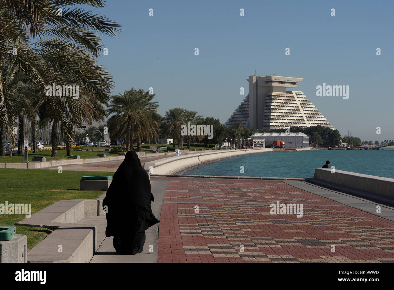 Arab woman walking along the  Corniche with the Sheraton Hotel in the background, Doha, Qatar Stock Photo