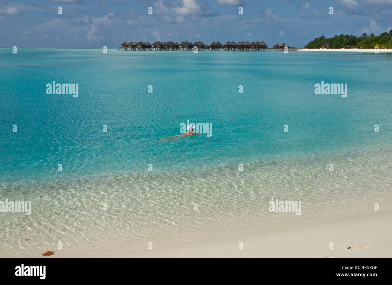 A lone young adult female swimming in crystal blue lagoon with water villas in background Stock Photo