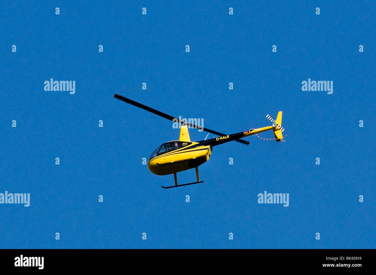 Black and yellow helicopter, Air Lloyd Robinson R44 Raven II, flying against a blue sky Stock Photo