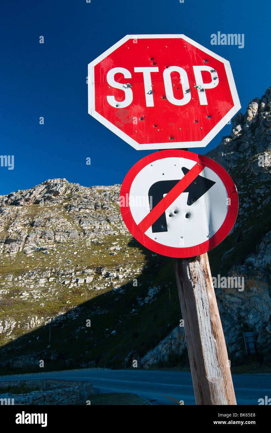 A stop sign and a right turn prohibited sign with bullet holes, with a rocky hill in the background.From South Africa. Stock Photo