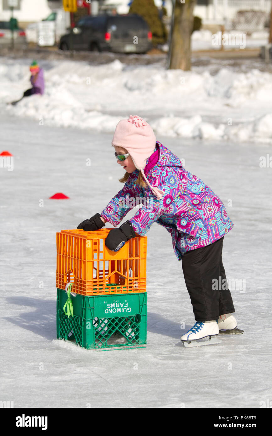 Young girl learning to ice skate with plastic milk crates in winter