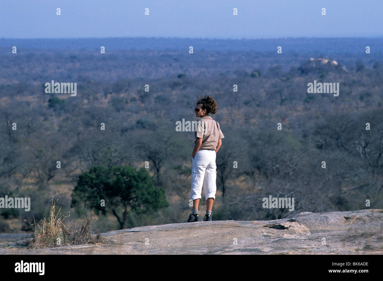 A female tourist scans the vast area of Kruger National Park from an elevated position above the savanna. Stock Photo