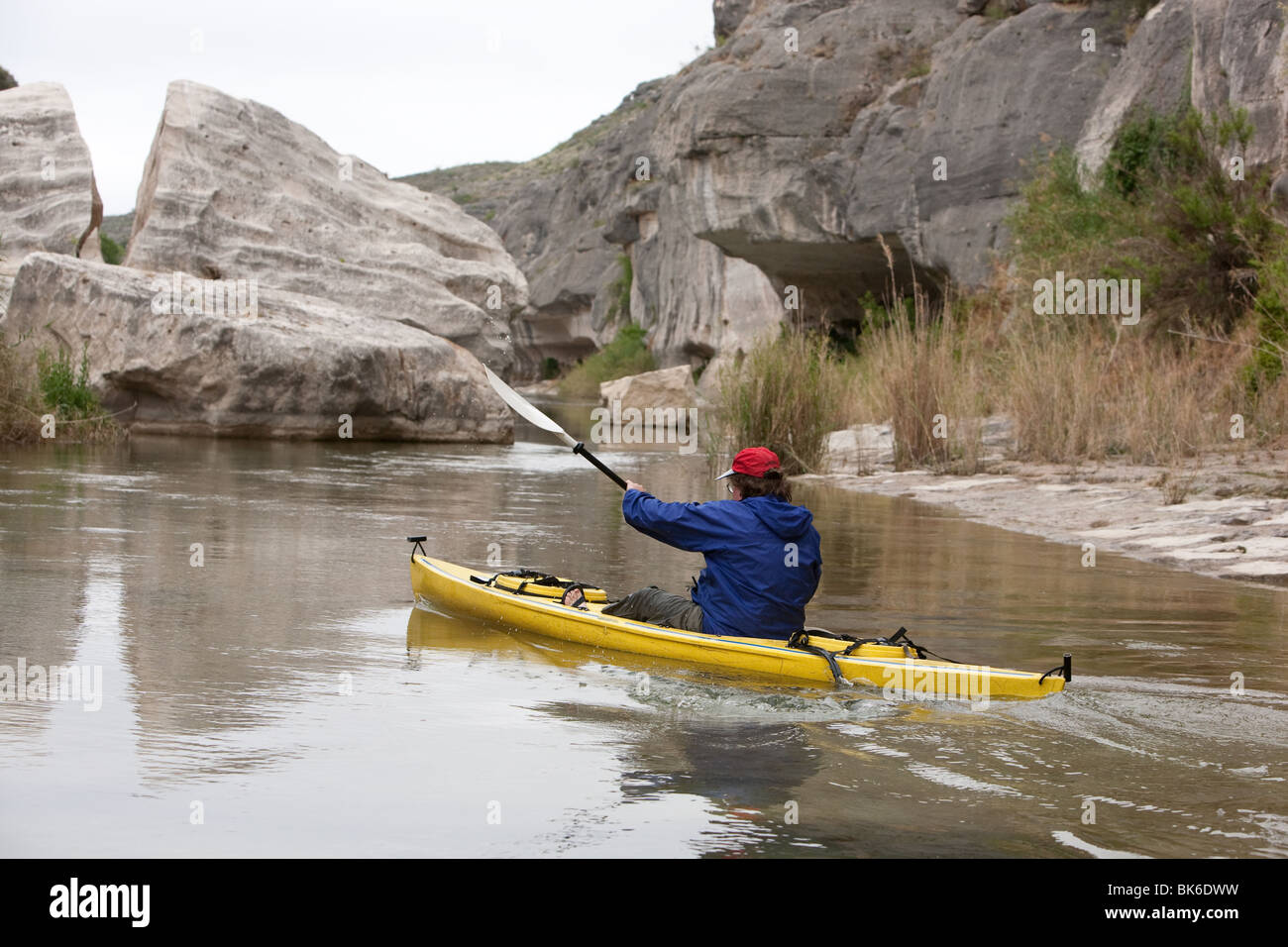 Man in solo kayak paddles by rocks on the Pecos River arm of Lake