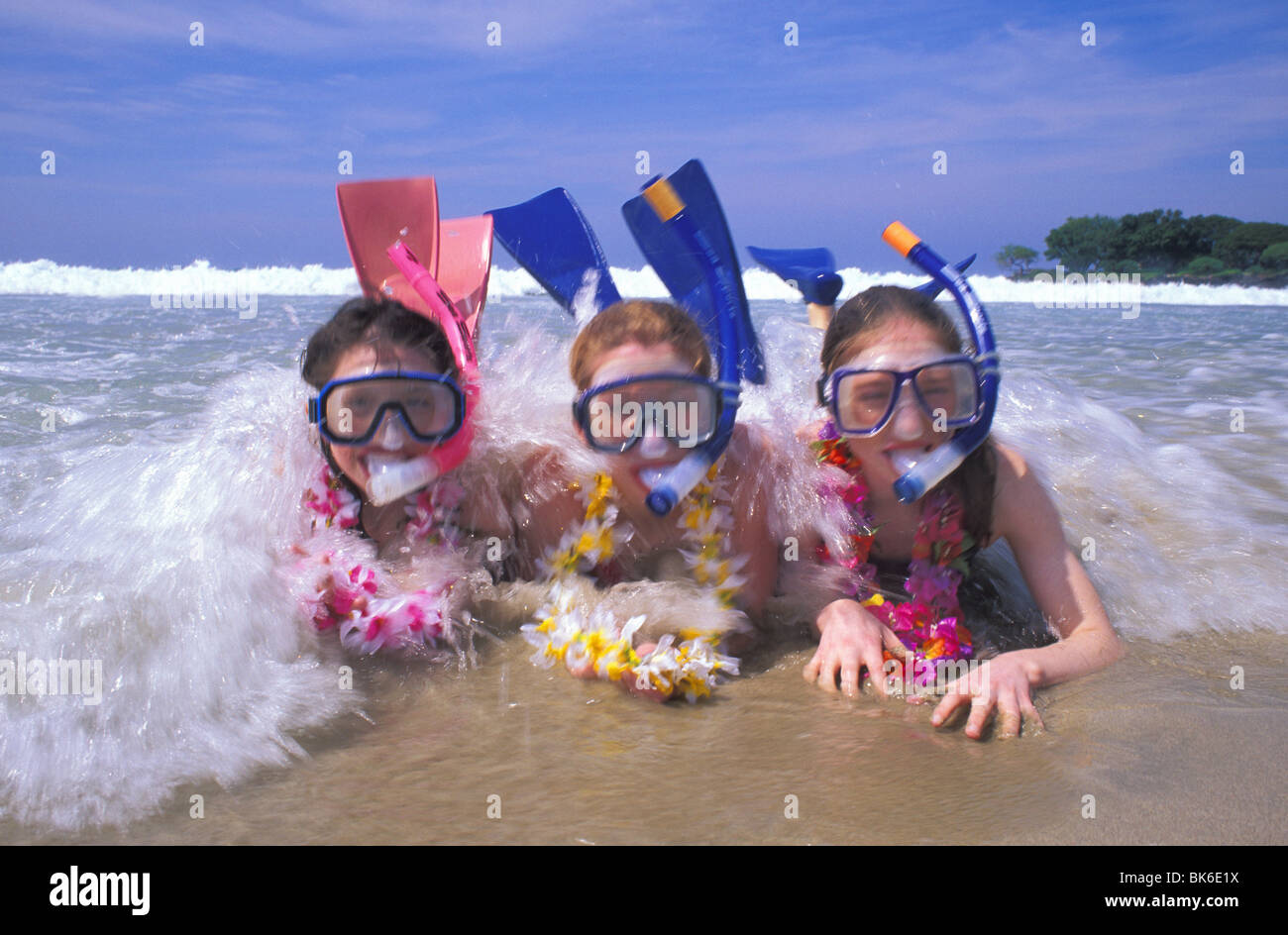released girls with snorkel gear wearing leis play in ocean surf Hawaii