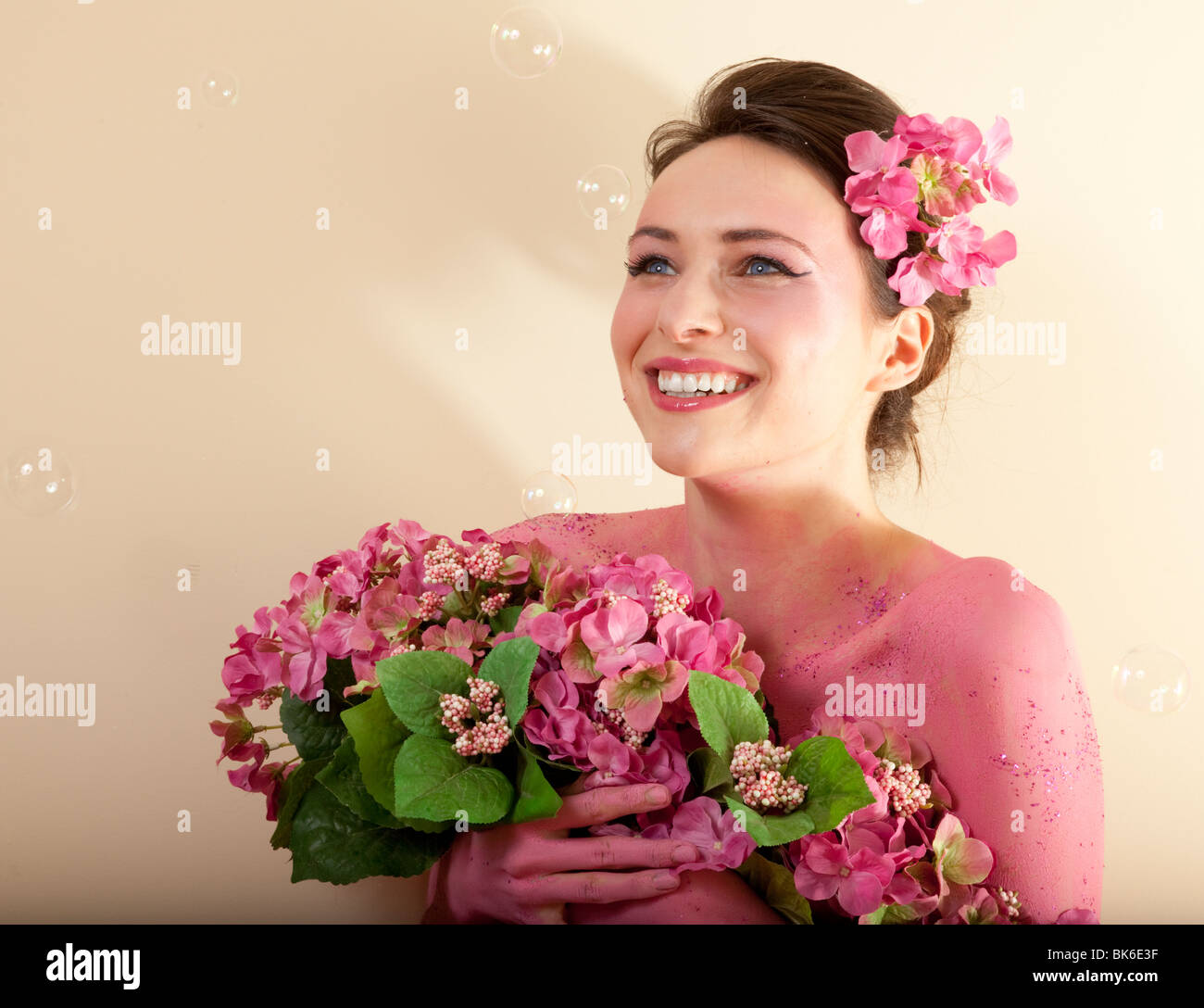 Studio photo of pretty brunette woman holding bouquet of artificial flowers, looking upward. Stock Photo