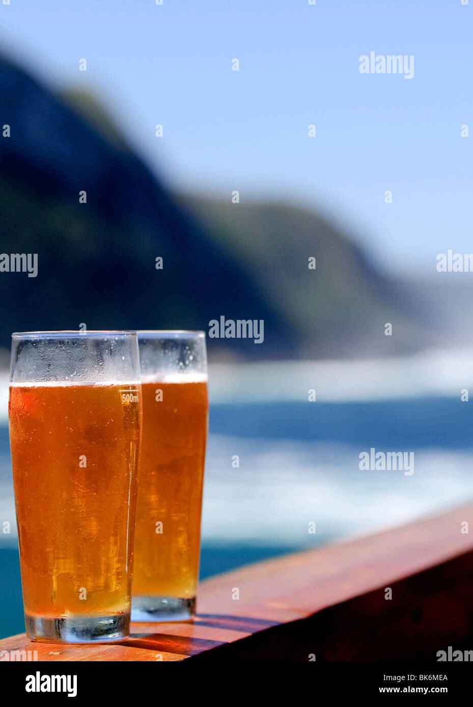 Two glasses of beer on a railing, with a dramatic coastline as ...