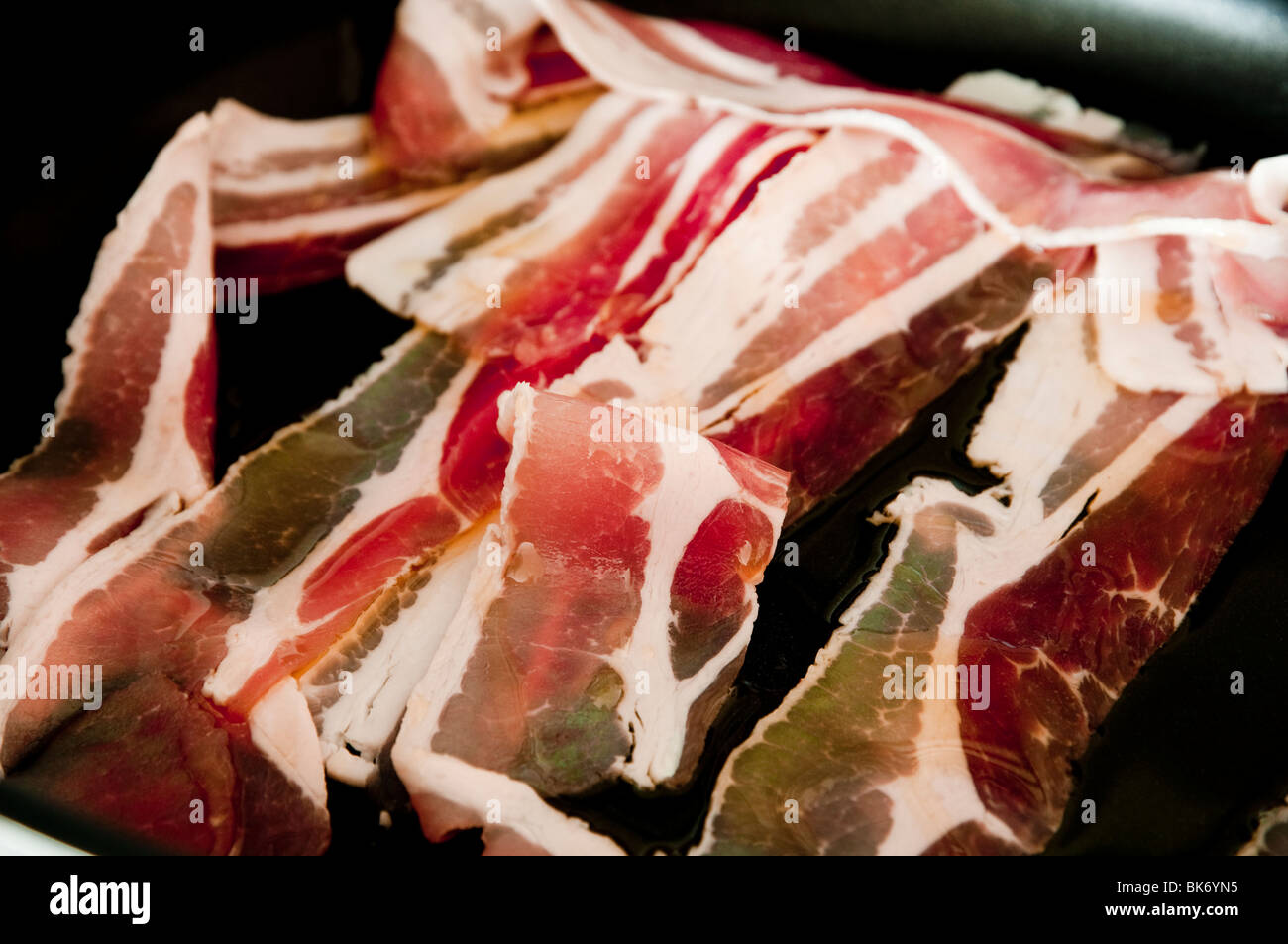 Rashers of bacon, raw and streaky bacon - being cooked / fried in a frying pan. Close up view. Stock Photo