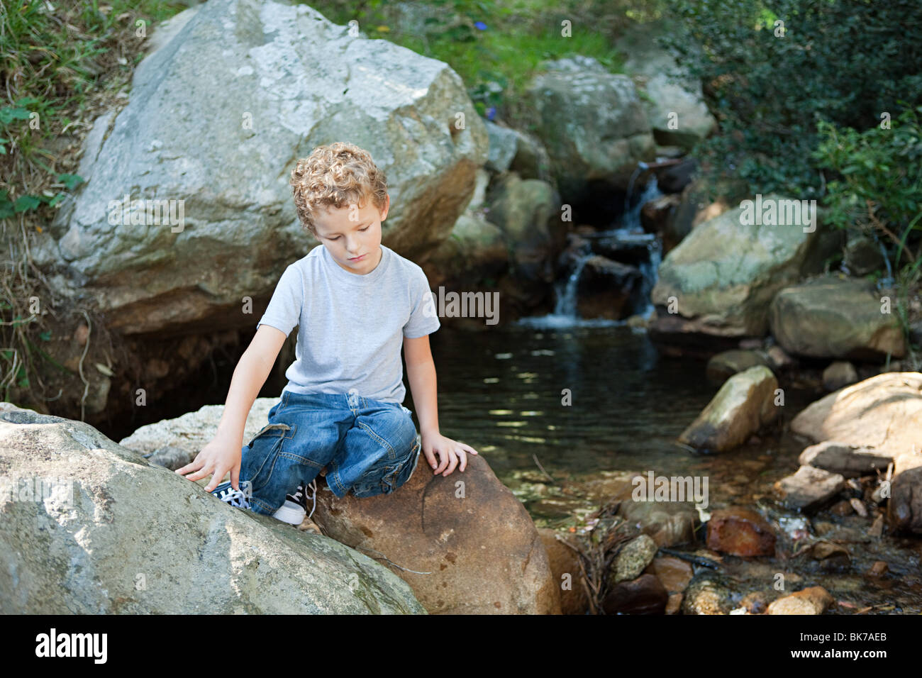 Boy sitting on rock by a river Stock Photo - Alamy