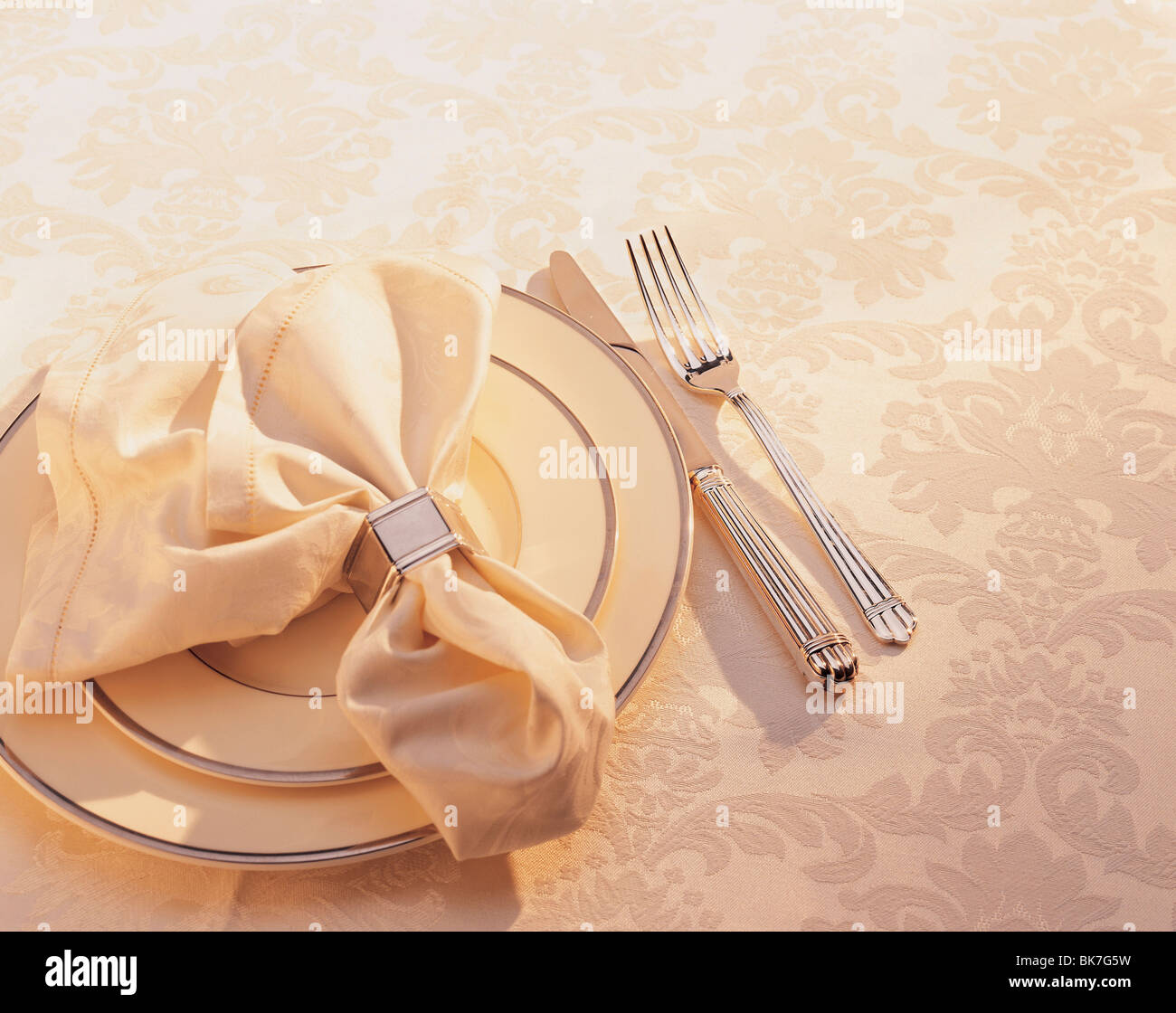 Napkin, plates and flatware on a yellow brocade table cloth with intense light. Stock Photo