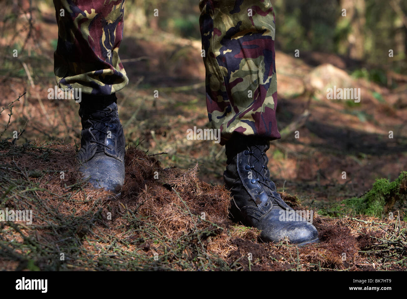man wearing camouflage combat trousers and boots standing guard blocking the way in a forest in the uk Stock Photo