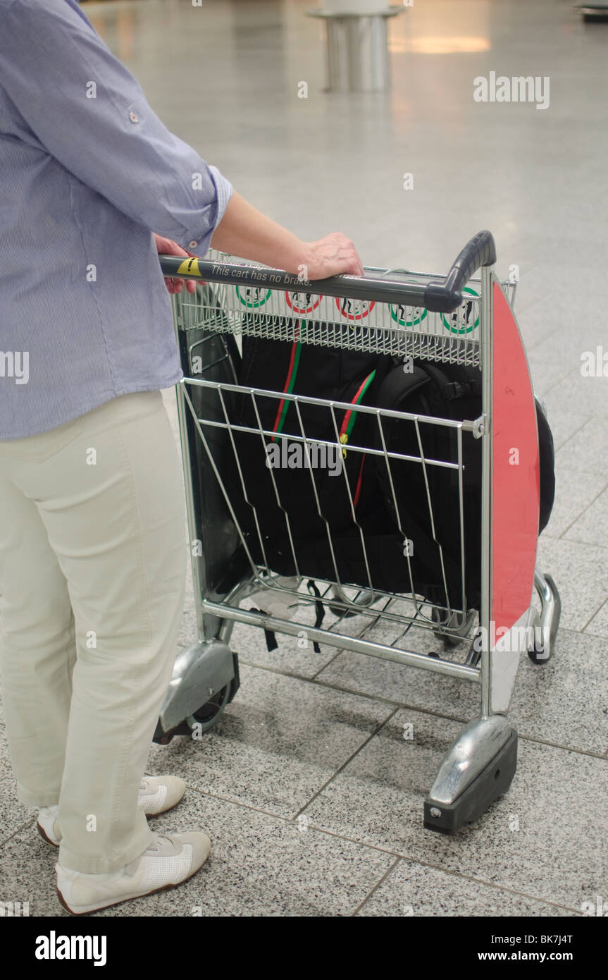 Woman on airport with luggage cart. Focus on cart Stock Photo